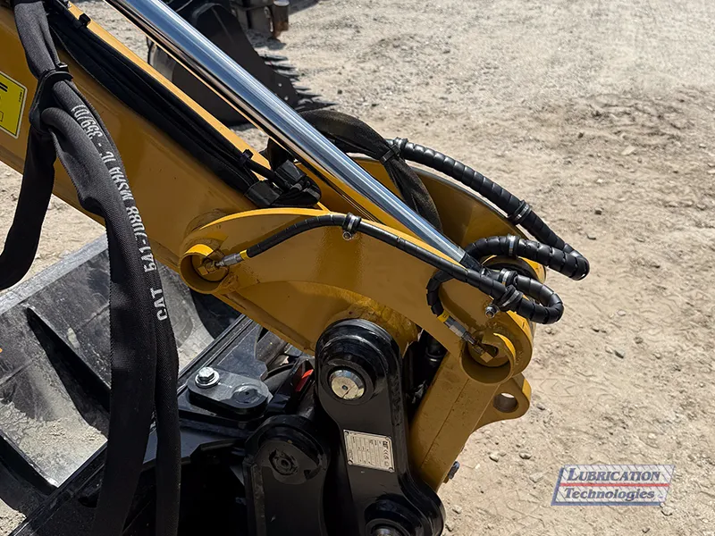 Close-up of tail lines from a ReliaMAX™ automatic lubrication system routed along the stick linkage of a CAT 305 Mini Excavator